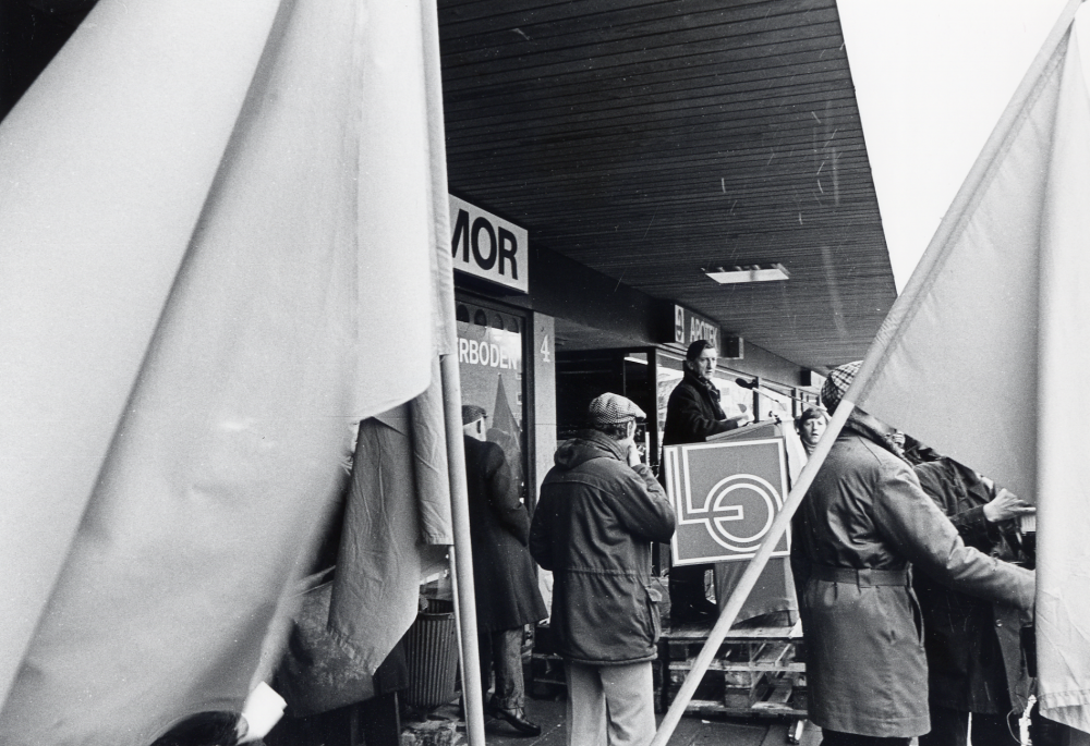 Sveriges arbetareparti m fl socialistiska partier i Vallentuna ordnar första maj-demonstration med samling bakom Centrumbio för att tåga till Tuna torg. Här har man kommit fram till Tuna torg och i talarstolen står Tore Pettersson omgiven av fanor
