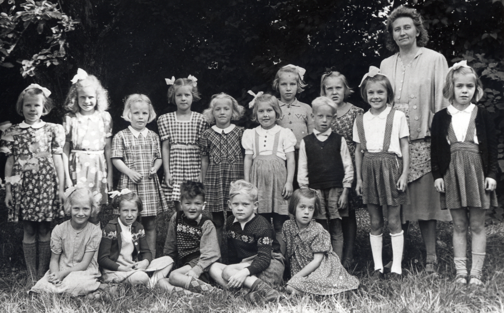 Lärarinnan Valborg Eriksson tillsammans med skolbarnen utanför Orkesta småskola.  I bakre raden fr v Kyllikki Teder, Margret Sporre, Ingrid Gustavsson, Marie-Louise Jansson, Vivian Lantz, Hillevi Andersson, Eivor Jansson, Bertil Lundwall, Ingvor Johansson, Birgitta Forsberg och Margareta Forsberg.  Nedre raden fr v Margareta Nordström, Viola ?, Hans Lindström, Ulf Carlsson och Maj-Britt Nilsson
