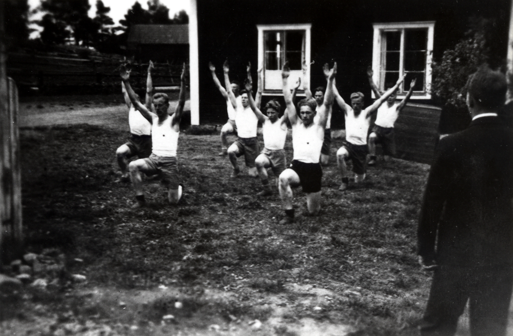 Provtagning för gymnastiktrupp-märket i GoIF Kåre.  Med ryggen mot kameran står ledaren och folkskolläraren Halvar Hedler.  GoIF Kåre hade såväl pojk, och flickavdelningar som dam- och herravdelningar.  Varje år avlades prov för gymnastikgrupp-märket.  Utomstående kontrollanter kom för att bedöma.  På planen (utanför Kyrkskolan?) deltar Åke Ahlgren, Åke Edlind, Helge Andersson, Lennart Johansson, Olle Edlind, Erik Lundberg, Gösta Jansson, Gunnar Jansson  och Georg Åhman