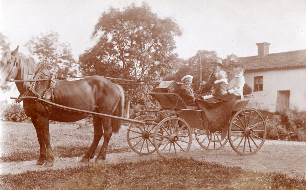 Ernst och Anna Jansson med barnen Gustaf, född 1917, och Anne-Marie, född 1918, på gårdsplanen vid Torsholma gård i Frösunda.  De sitter alla i en landå, dragen av en häst