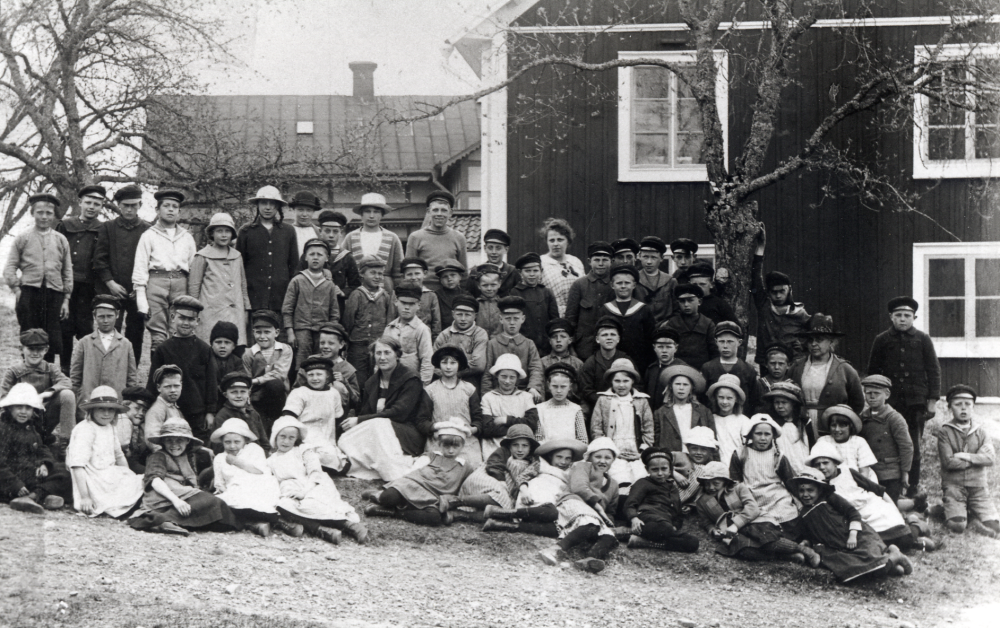 Kyrkskolan i Lilla Garn, Össeby-Garn.  Bakre raden fr v ? Birgersson, Artur Johansson, Lennart Karlsson,Sven Karlsson, Verna Samuelsson gift Johansson, Ester ?, Ingeborg Vallbom, Arne Karlsson, okänd, ? Forsberg, ? Eklund, Sixten Lundström, lärarinnan Rut Nilsson, Torsten Wallin, okänd, Nils Alstermark och Bengt Almén.  Stående rad 2 Valter Andersson, ? Ekström, okänd, ? Ek, okänd, Olle Ekstam, Sven Dahlbeck, okänd och Evert Johansson.  Rad 3 börjar längst ut t v Georg Dahlbeck, okänd, ? Ek, Gösta Hoffman, okänd, här fortsätter rad 2 över lärarinnan, ? Nilsson, Erik Svärd, Sture Jonsson, okänd, ? Karlsson, Gunnar Petersson, Rolf Sundström, okänd,  lärarinnan Matilda Lindhe och Tore Källström.  Sittande längst ner fr v i mörk kappa och vit hatt ? Nilsson, Britta Börjesson, Gösta Olsson, Harry Karlsson,  Robert ?, Elsa Lönn,  lärarin- nan Nanny Skoglund, okänd, Ester? Jonsson, Doris Wallin, okänd, Svea Lundström, okänd, Magda Westling, Karin Andersson Stora Karby, Sigurd Dahlbeck och Sven Andersson på knä.  Sittande allra längst fram börjar med flicka i mörka kläder  och mycket stor hatt  Karin Nilsson,  4 okända, Maja-Lisa Almén, 4 okända, Svea Karlsson med randigt förkläde och ? Kraemer Arken liggande i mörk klänning med ljus hatt med mörkt band samt  okänd.  Totalt 72 skolbarn