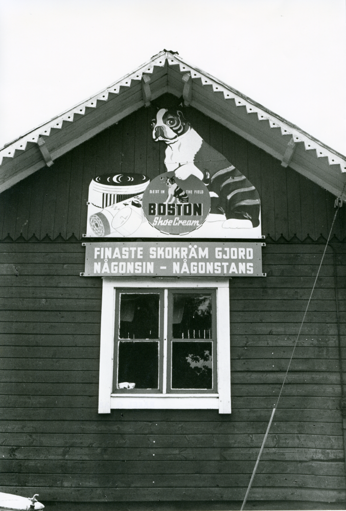 Sista dagen för handlarfamiljen Karlsson i Frösunda handel. Skylt på fasaden med reklam för Boston skokräm.
•Fotografiet ingår i bildserien ”Vardagsliv i Vallentuna kommun” av Rachael Gough-Azmier & Gunilla Blomé, Haga Studios HB.
