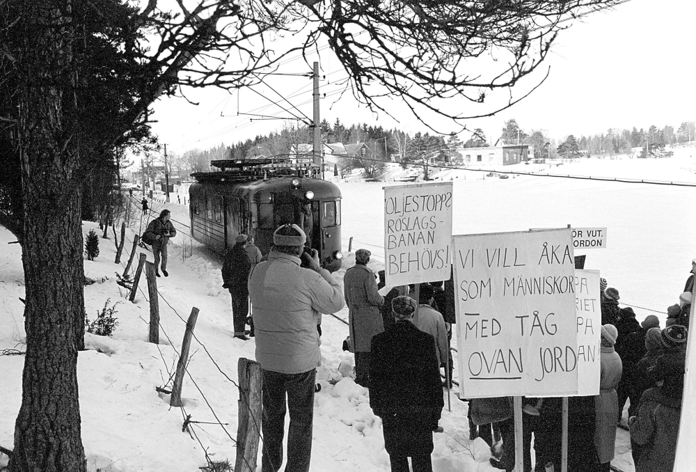 Protester inför hot om nedläggning av Roslagsbanan;  Föreningen Rädda Roslagsbanan protesterar inför hotet av nedläggning av järnvägen. Trafiken Kårsta-Rimbo upphörde i januari 1981.
I bakgrunden skymtar Kårsta stationshus och t.h. det gamla affärshuset Österlid, sedan 1969 ombyggt till bostad för familjen Staff.