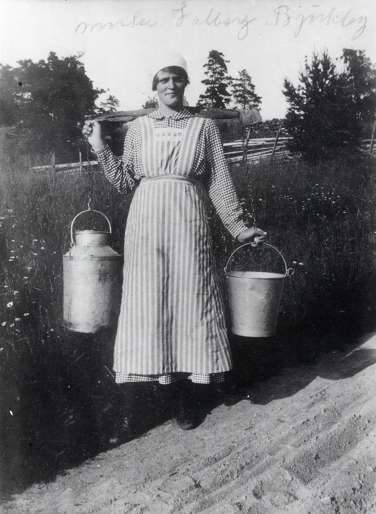 Valborg Gustafsson  från  Björkby gård  bär en mjölkflaska och en hinkar med ett ok.  Valborg levde 1900-12-05–1920-04-12
