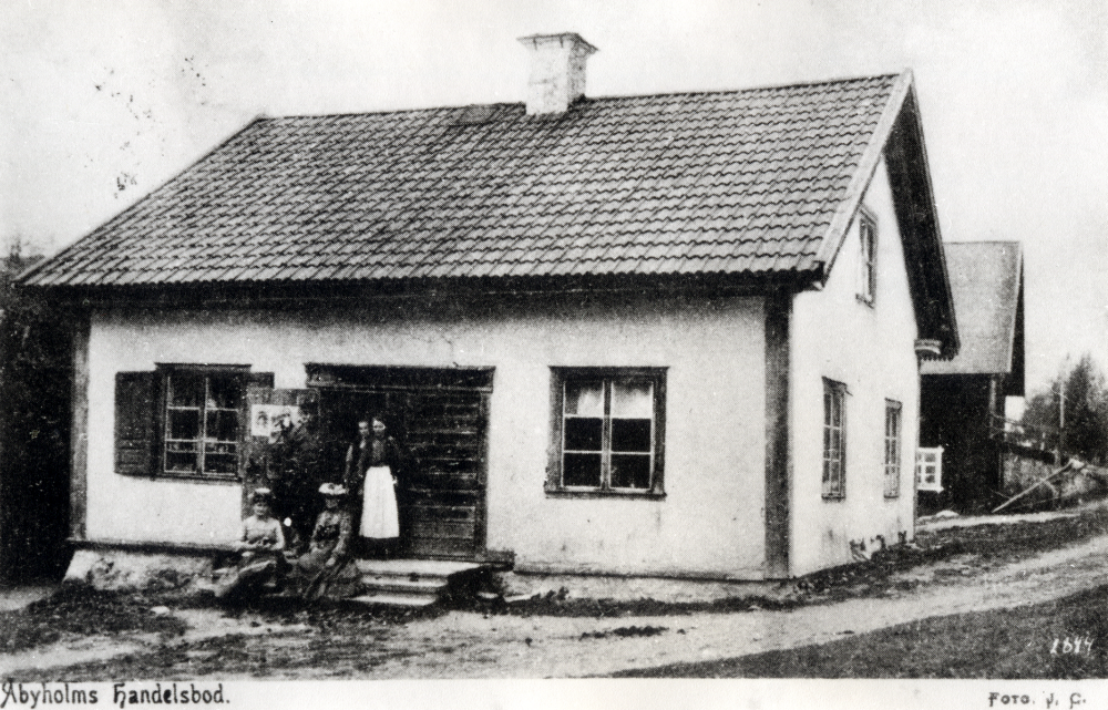 Åbyholms handelsbod låg i den norra flygeln vid Åbyholms gård Jacob Jacobsson köpte gården 1863, fortsatte med gästgiveriet som funnits i gården sedan tidigare och inredde en handelsbod i norra flygeln. Affärsrörelsen lades förmodligen ner ca 1910, sedan sonen Knut Jacobsson drivit handeln omkring 1904. En påse med hans namn återfanns vid restaureringen av Åbyholms gård.
Foto förmodligen Zackeus Carlsson, initialerna felskrivna på vykortet