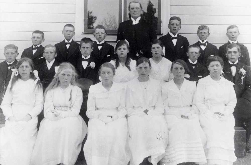 Konfirmation i Vallentuna kyrka. Prosten Pettersson tillsammans med konfirmanderna. Pojkarna fr v okänd, okänd, B Söderberg, ? Glassel, Karsten ?, okänd, Sven Karlsson Väsby, okänd, Nils Vestberg, okänd, Johan Lindberg Tallhammar med blommor på kragen. Flickorna fr v okänd, Greta Lönn, Lilly Johansson, Signe Österberg Vallby, Anna Andersson Nähle, Stina Öberg, Märtha Stav Grana och Rut Söderberg