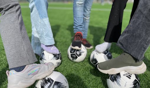 Elever som står på fotbollsplan och står med fotboll under fötterna.