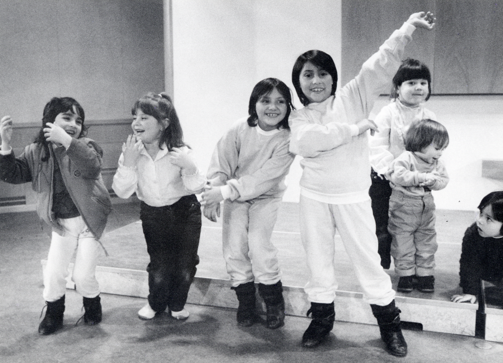 Invandrarafton med musik och dans i Vallentunasalen. Fyra små flickor 'dansar' vid podiet.  Tre mindre barn är bredvid