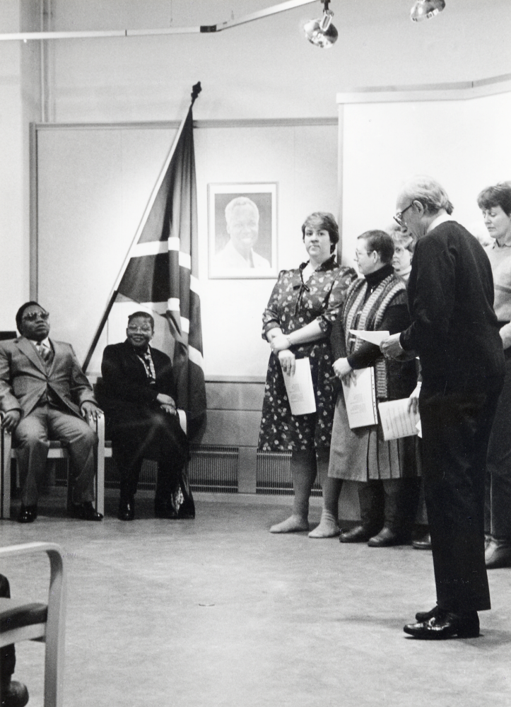 Tanzania-utställning i Vallentunasalen 16 februari till 2 mars 1985. Arrangör var Vallentuna församling. Utställningen invigdes den 16 februari kl 12 av Tanzanias ambassadör i Sverige D N Mloka med hustru. De sitter t v vid landets fana och lyssnar till Åke Carlestam. Kvinnorna fr v är Maria Stjernberg, Christina Servin? okänd och Ingrid Rost