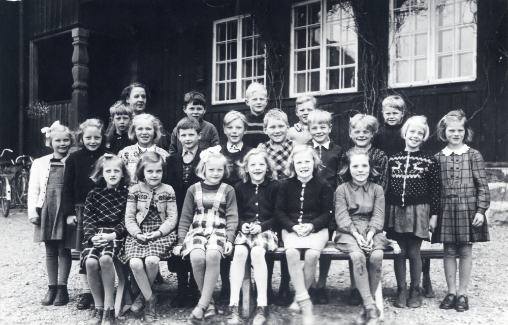 Klass 1 i Hjälmsta skola utanför Röda skolan tillsammans med lärarinnan Berna Nilsson. Med på bilden är (oklar ordning) Gunborg Jansson, Mona Bergström, Birgitta Bengtsson, Ulla Brohlin, Ulla Leverin, Lage Jansson, Olle Linblom, Rune Lundkvist, Bertil Wahlberg, Ingegärd Tillborg, Harriet Raab, Bengt Nyberg, Gunvar Nilsson, Tommy Karlsson, Siv Österberg, Ralf Sundkvist, Harry Wennberg och Kjell Pettersson
