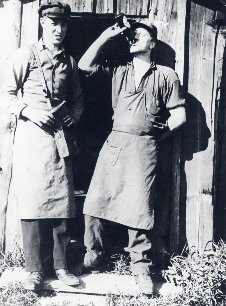 Skomakare David Lund  t h tar sig en öl utanför skomakarestugan mittemot  Karlsbergs affär.  Bredvid står ölutköraren  Sabel  från Upplands Väsby. Öl fick inte säljas i affären, varför en bryggarbil körde runt och sålde öl i gårdarna. Efter en stormig omröstning i kyrkskolan beviljades tillstånd för ölförsäljning 1948.  Drängstugan som inrymde skomakarverkstaden revs 1943.