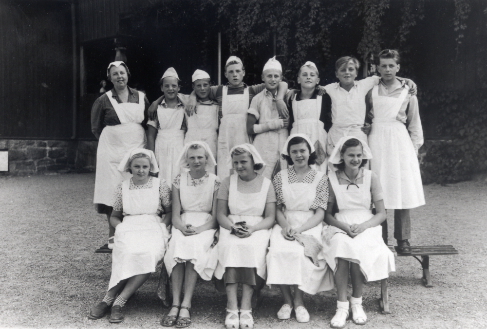 Fortsättningsskolans elever i klass 7 har skolköksundervisning i Röda skolan.  I bakre raden står fr v  Rune Jakobsson, Gösta Jansson, Bert ?(bodde i Veda),  Bengt Lutteman, Ulf Bengtsson, Lennart Karlsson och  Yngve Landin.  Sittande fr v Kerstin Frej, Britt-Marie Grip, Inga-Maj Hoff, Alida ? och Viola Wester (Wrese).  Lärarinnan kom från Stockhollm och ledde fortsättningskolans skolköks-undervisning. Eleverna hade enbart hushållskunskap på schemat  under de veckor under sommaren då fortsättningsskolan pågick