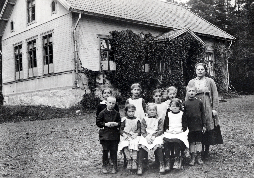 Lärarinnan Lisa Barthelsson tillsammans med skolbarnenutanför Sunnanå småskola. Nedre raden fr v Sven Widegren, okänd, Hedvig Johansson, Gun Pettersson och Sven Eriksson (Keller).  Övre raden fr v okänd, okänd, Margit Helgöstam, okänd.