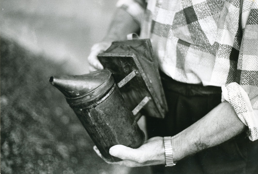 Biodlare Thitus Hahn på Åbyholmsvägen i Vallentuna arbetar med honungsskörden. Här håller han i rökpusten. Thitus Hahn var tidigare trävaruhandlare.
•Fotografiet ingår i bildserien ”Vardagsliv i Vallentuna kommun” av Rachael Gough-Azmier & Gunilla Blomé, Haga Studios HB.