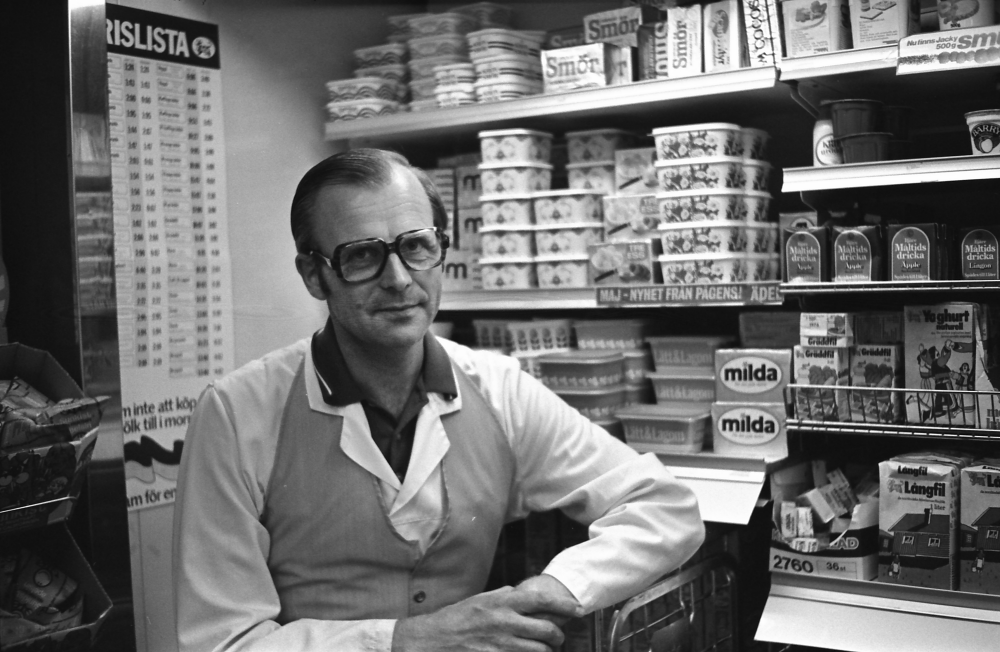 Handlaren vid Ica Rickeby 1976, namn?Den 22 februari 1973 blev "Sivertssons livs" "Ica Rickeby". Ica Rickeby låg på Skolvägen 1, nedanför Karlbergsvägen. Ica-butiken lades ner i slutet av oktober 2017. 
•Fotografiet ingår i bildserien ”Vardagsliv i Vallentuna kommun” av Rachael Gough-Azmier & Gunilla Blomé, Haga Studios HB.
