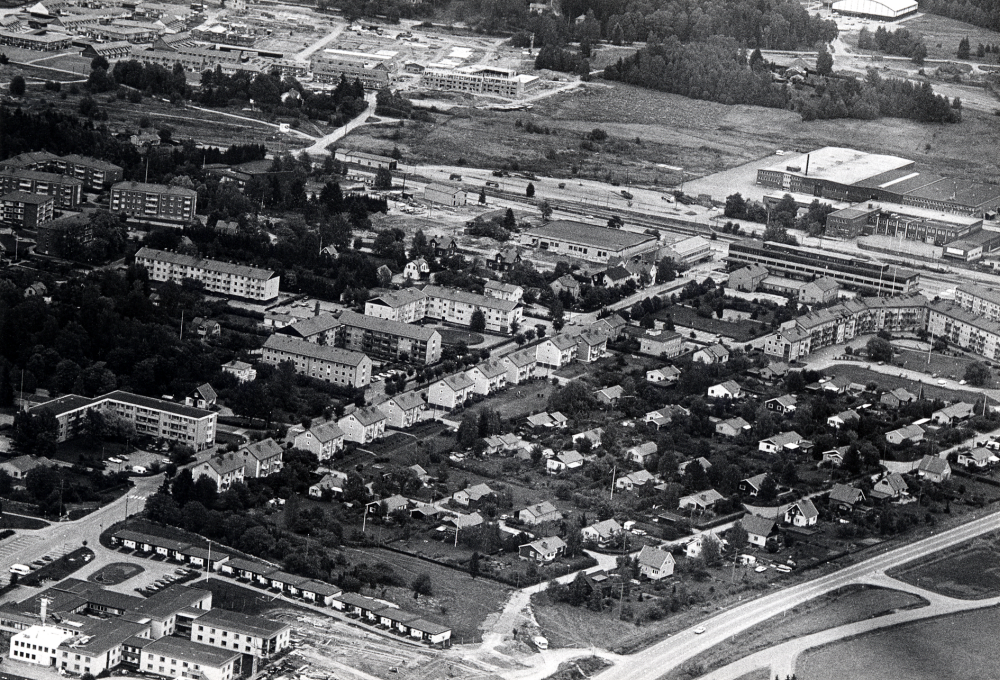 Flygfoto över Vallentuna centrala delar med Prästgårdsgärdet i förgrunden. Längst ner t v Väsbygården. Längst upp t h Tellus-Maskin med Tunahuset och Vallentuna centrum framför. Längst upp i hörnet t v pågår byggnadsarbeten med Åby gärde. I hörnet längst upp till höger syns sporthallen I bildens mitt bostadsrätter  längs Allévägen