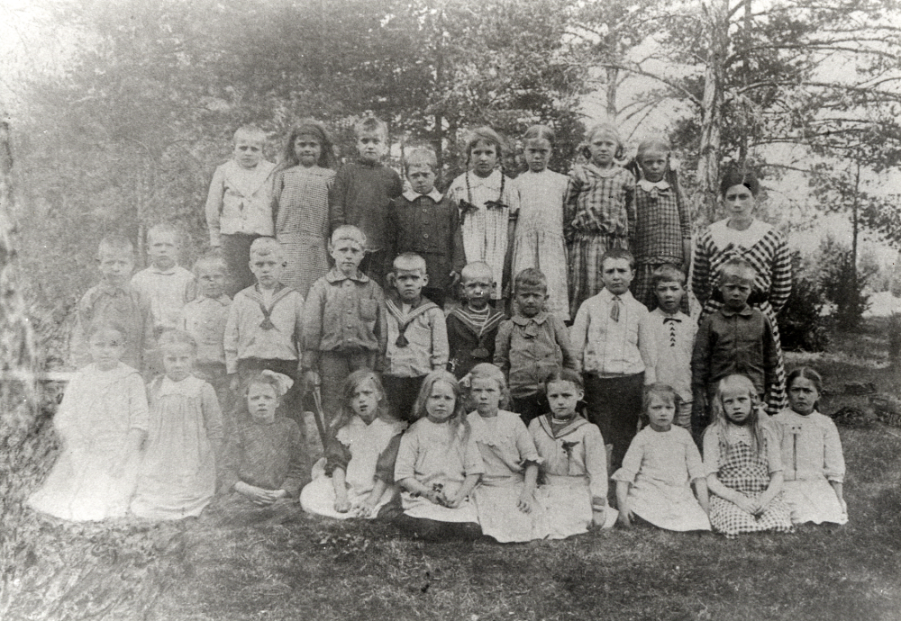Lärarinnan Anna Gauffin med skolbarnen vid Hjälmsta skola.Bakre raden fr v nr 3 Evert Johansson, nr 6 Linnea Krieg.  Mittenraden fr v nr 17 Herbert Karlsson, nr 18 Åke Lindström, nr 19 Helge Henningsson, nr 25 Maja Bergman (gift Jansson), nr 26 Ella Jansson och nr 29 Tyra Fälldin