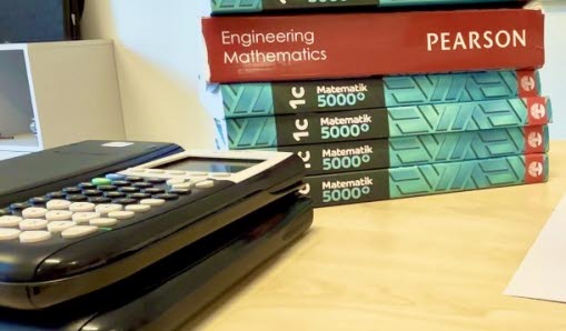 Undervisningsböcker som staplats på barandra och intill finns miniräknare.