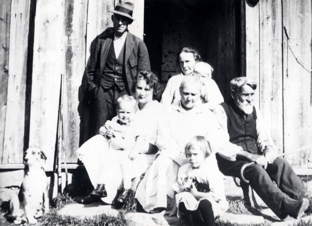 På trappan vid Gamla stugan i Bäcken sitter fr v Sten Berggren, Julia Berggren med Harry i knäet, Siri Berggren med Rune i knäet, Ida Berggren. Fredrik Berggren och den lilla flickan med en kattunge i famnen är Inga Berggren, (senare gift Åkerblom).  Hunden heter Staffi