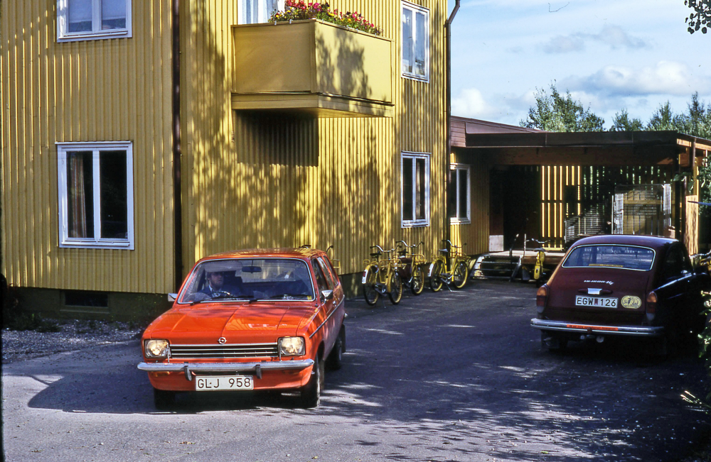 En arbetsdag med lantbrevbärare Mikael Mattsson. Brevbärarexpeditionen på Olsborgsvägen; Brevbärarexpeditionen på Olsborgsvägen, som revs 2009. Lantbrevbärare Mikael Mattsson i orangebil till vänster. Wolksvagen till höger ägde Gunnar Jansson som körde ut post i västra Vallentuna och Lindholmen. Fram till 1990 höll lantbrevbärarna med egen bil. 