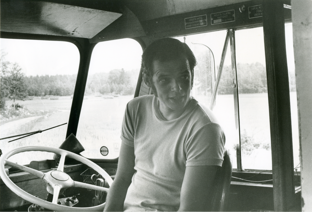 Arne Karlsson, som kör livsmedelsbussen från Frösunda handel, sitter i bussens förarhytt. 
•Fotografiet ingår i bildserien ”Vardagsliv i Vallentuna kommun” av Rachael Gough-Azmier & Gunilla Blomé, Haga Studios HB.
