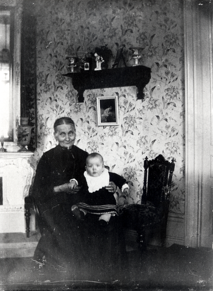 Johanna Carlsson, förmodligen i hemmet i Jönköping med barnbarnet Sven Karlsson i knäet.  Familjen flyttade till Väsby gård i Vallentuna när maken, byggmästaren,  B C Carlsson köpte gården 1906