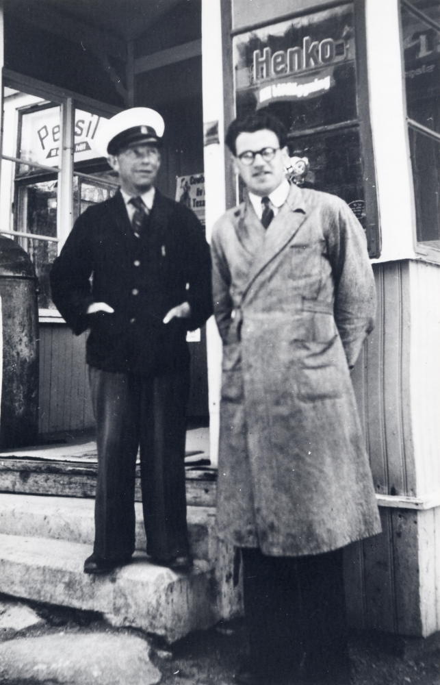 På trappan till  Karlborgs handeslbod  står t v  Post-Pelle,   Helge Karlsson  och t h bodbiträdet  Bengt Andersson.  T v i farstun står en  fotogentunna  ur vilken fotogen såldes