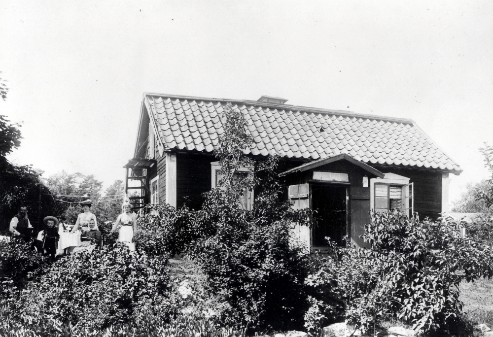 Eriksdal, Nyborg vid Solsta i Frösunda. Vid stugan står fr v skomakare Ekström (-1917), fostersonen Carl de Pellegrini, fru de Pellegrini, Matilda Ekström (1849-03-25-1941) och fosterdottern Gerda. "Sedan tant Ekström dött köptes huset av Holmbäck, som avled 1955". Huset finns kvar 1989