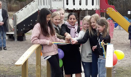 Grupp barn som står på varsin sida om en kvinna. Tillsammans klipper de av ett blågult band.