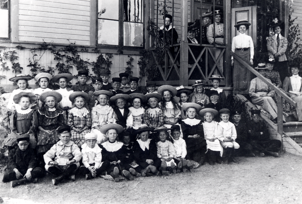 Examen  i  Sunnanå skola.  På trappan står fr v nr 2  fru Rask  nr 4  fru Johansson  på Helgö, nr 5 lärarinnan  Lisa Barthelsson  nr 6  Gunhild Carlsson-Waldebäck.  Barnen i bakre raden fr v nr 1  Anna Lisa Carlsson  nr 3  Gertrud Johansson  nr 6  Rut Pettersson  nr 7  Helgöstam  nr 8  Sven Helgöstam  Mittenraden fr v nr 5  Helga Helgöstam  (Céwe) nr 11  Sara.  Sittande fr v nr 1  Helge Andersson  nr 2  Manne Edman  nr 3  Bo Carlsson  (Waldebäck), nr 4  Eva Lundkvist  gift Pettersson, nr 7  Viran Gustavsson  gift Österberg, nr 9  Rut Lundkvist  nr 11 dotterson till fröken Barthelsson, nr 12  Nils Carlsson (Waldebäck)