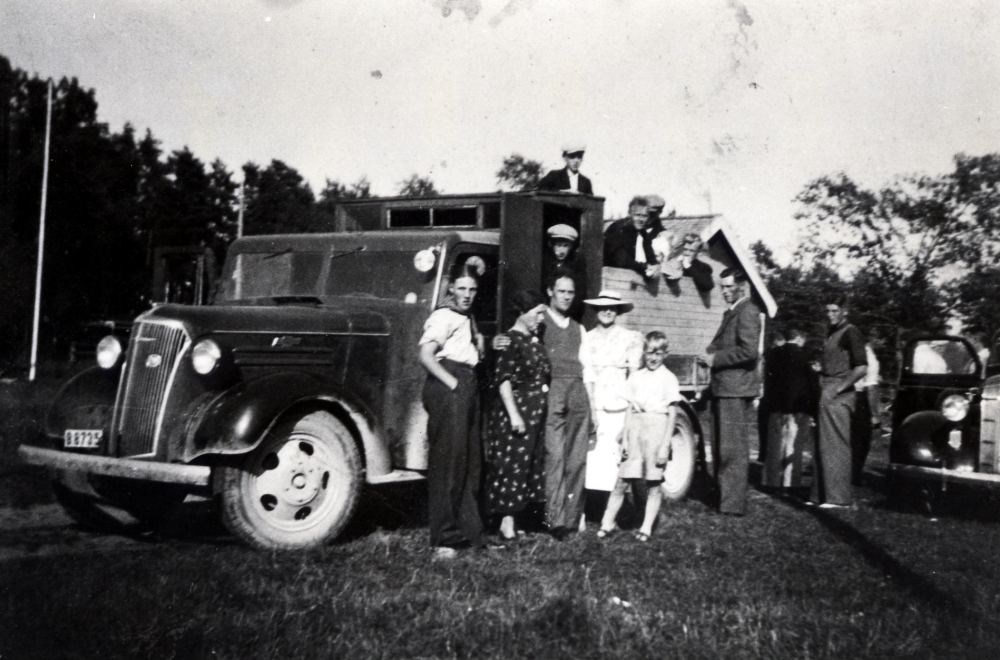 Fritz Johansson hade åkeri och ägde en lastbil av märket Chevrolet.  På flaket hade en kur byggts.  Fritz  (avled 1936) och hans son Lennart körde varor från de olika trädgårdsmästerierna, t ex  från Kårsta (Edlinds), Ekskogen (Karlssons), Ormgården (Anderssons) och ibland också från Ella trädgård i Täby.  I kuren kunde torgdamerna stå utan att bli vindpinade under färden mot Stockholm och Östermalmstorg  Varorna placerades på flaket.  Lastbilen kunde också användas för transporter av ungdomar till olika idrottsevenemang, som här, förmodligen en orienteringstävling i Össeby.  Främst står Kurt Johansson, damen i hatt heter Andersson och mannen i kostym Gustavsson från Frösunda