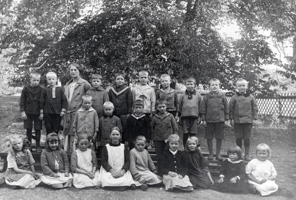 Klasserna 1 och 2 i Össeby-Garns kyrkskola. Bakre raden fr v Martin Vesterberg Uddralund, John ?, lärarinnan Nanny Skoglund, Hans Karlsson Brottby, Svante Karlsson Malmbacken, Nils Johansson Hakunge, Edvin Lönn, Edvin Nordgren Toftesta, Nils Eriksson och Walter Dahlbeck Ösby. Mellanraden fr v Valter Andersson Sundby, Gunnar Dahlbeck Ösby, Tore Eriksson Norrdal, ? Berggren Prästgården/Frukthammar. Sittande fr v Märta Karlsson Karby, Birgit Lundgren Hakunge, Iniz Berggren Frukthammar, Svea Svärd Olunda, Ketty Johansson Sjötorp, Anna-Lisa Wallbom Skogsberga, Anna-Lisa Fernström Forsenberg, Linnea Westin Karby och Britta Levald Klockargården