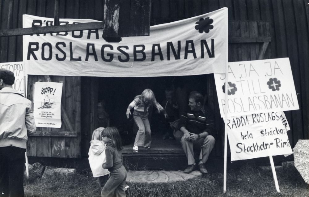 Centerpartiet har valmöte vid Väsby kvarn Här står en banderoll lutad mot kvarnen med texten Rädda Roslagsbanan och plakat med text 'ja, ja, ja till Roslagsbanan. Små flickor hoppar ut från kvarnen