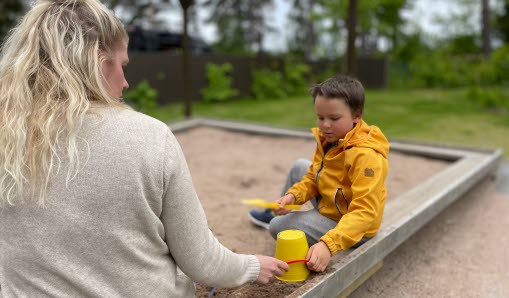 Elev sitter med pedagog i sandlåda och skapar sandhus tillsammans