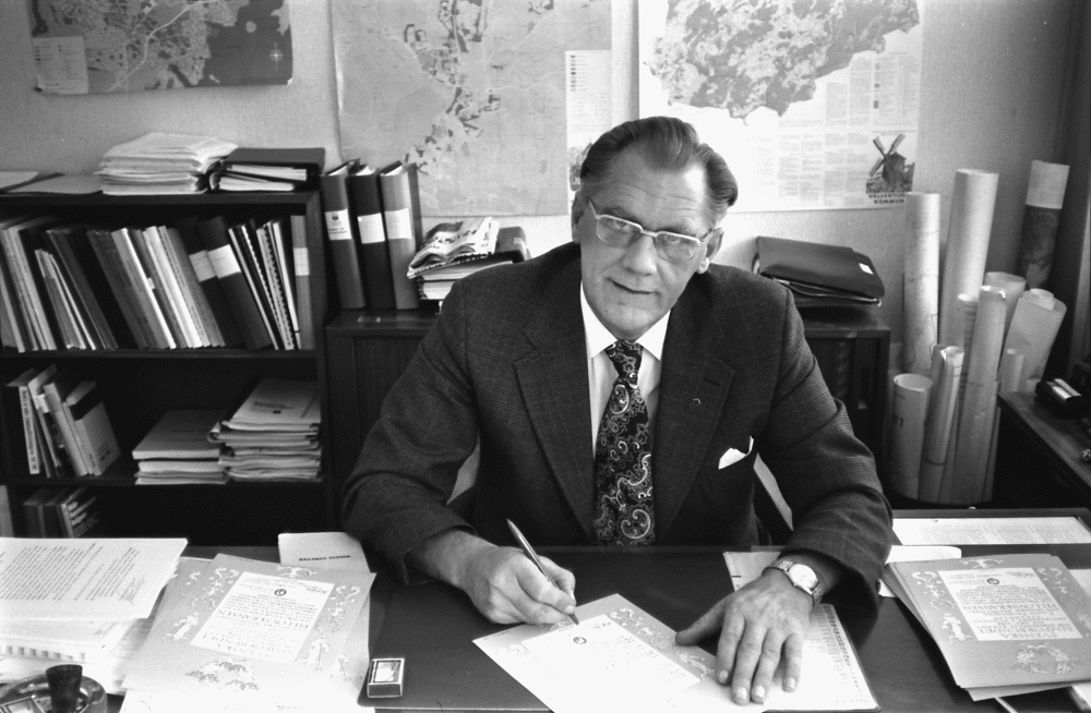 Kommunalrådet Karl-Erik Wikström (C) på sitt kontor signerar diplomen med Pillövskransen från Svenska Simförbundet som tilldelas deltagarna för "skicklighet i simning".
•Fotografiet ingår i bildserien ”Vardagsliv i Vallentuna kommun” av Rachael Gough-Azmier & Gunilla Blomé, Haga Studios HB.
