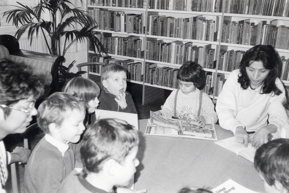 En grupp barn från  Granåsa daghem  besöker  Vallentuna bibliotek  och tittar i bilderböcker på barnavdelningen. Vid bordet sitter   Laleh Toosie  som bl a har hand om de persisktalande barnen