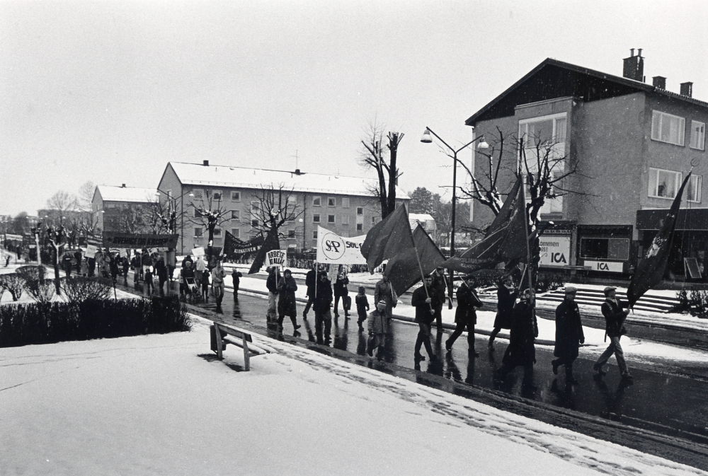 Sveriges arbetareparti m fl socialistiska partier i Vallentuna ordnar första maj-demonstration med samling bakom Centrumbio för att tåga till Tuna torg. Här går man längs Allévägen och är nästan frammae vid Mörbyvägen. Möjligen har man samlats först vid Sörgårdstorget för att tåga Allévägen ner mot centrum