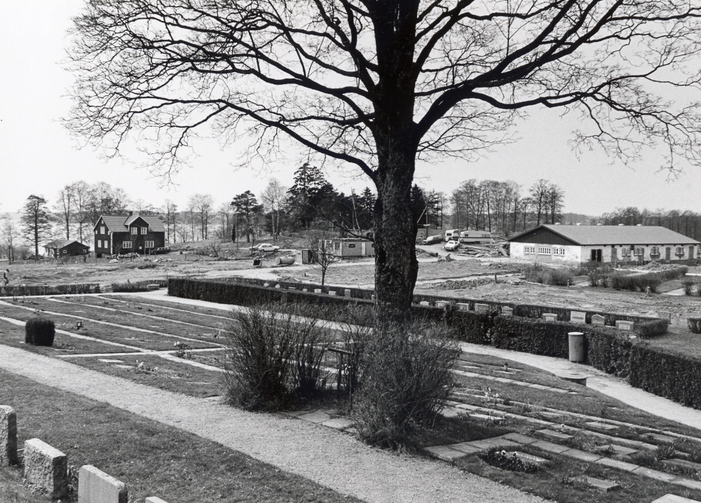 Vallentuna kyrkogård utökas mot väster. T v syns Sjövillan, t h ligger Prästgårdens ladugård, i bildens mitt syns redskapbodar m m från anläggningsarbetet. Foto från gamla kyrkogården t v om kyrkan