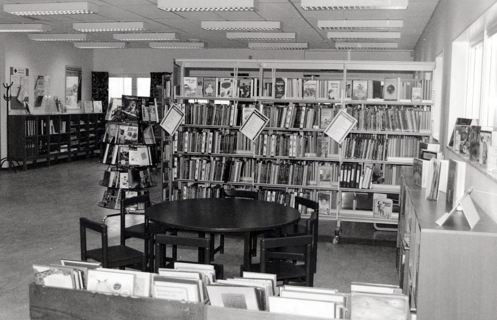 Karby bibliotek i samverkan med ICA Brottbyhallen vid Karby torg.  Biblioteket flyttade från Tallstigen 1994 och öppnade här i postens gamla lokaler.  Från början drevs biblioteket, posten och ICA i samverkan.  Posten flyttade efter några år till Bilisten vid Brottby torg.  2003 fräschades bibliotekslokalen upp med bl a ny färgsättning och nytt arbetsbord.  Här är barnhörnan med med nya barnmöbler.  I bakgrunden skymtar tidskrifthyllan och i förgrunden bilderbokstråg