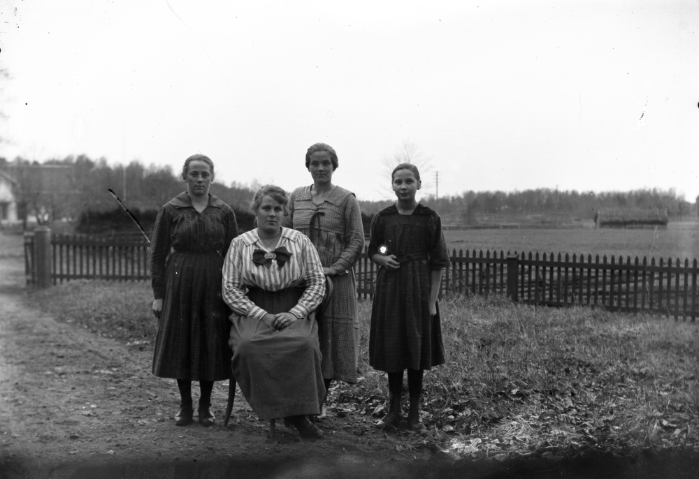 Fyra kvinnor framför ett staket. Platsen är okänd. Uppgift om fotoår saknas, men troligen 1920-talet.