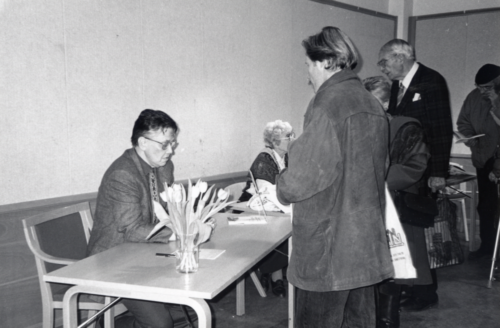 Boken Tio röster om Vallentuna sammanställd av Svante Berg presenteras och förstadagsförsäljs i Vallentunasalen.   I salen finns utställningsskärmar med fotografier ur Vallentuna bildarkiv. Program vid invigningen var "Att växa upp i Vallentuna" – Sylvia Pettersson berättar om sin uppväxt  på 1930- och 1940-talen.  Kulturnämndens ordförande Johan Mossling presenterar boken.   Här skriver Svante Berg dedikation i en bok till Lars Sjösvärd.  Vid bordet t h sitter Gunhild Nylén Hillbo i Vallentuna biblioteks vänner