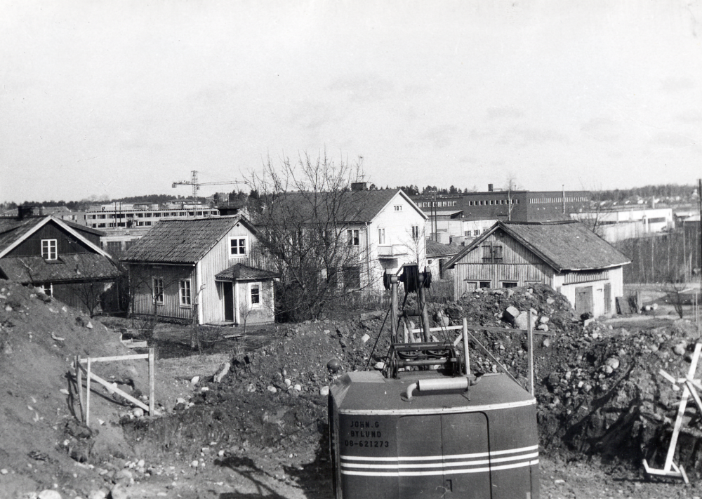 Arbeten i Trekanten vid Olsborgsvägen Framnäs-tomten styckas och bebyggs med flera villor. I bakgrunden under lyftkranen reser sig Tunahuset och t h syns Tellus-Maskins lokaler. I förgrunden bakom grävskopan ligger Konsums f d affärslokaler