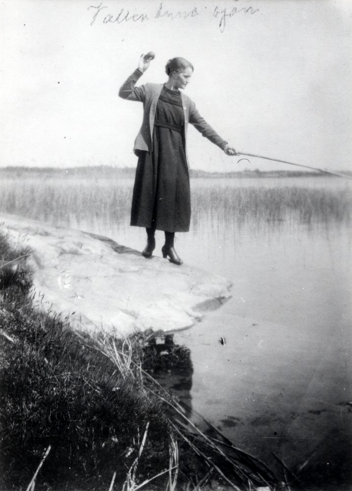 Ester Jansson vid Vallentunasjöns strand. I handen håller hon ett metspö? i den andra handen ett äpple?