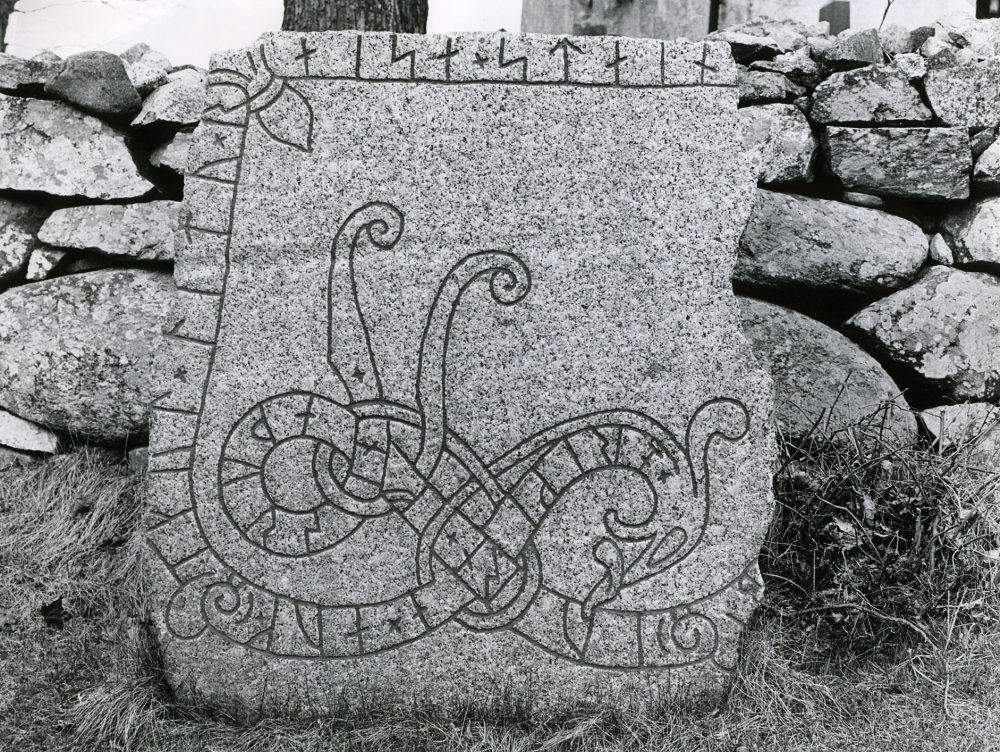 Runsten med beteckningen U202. Stenen restes 1938 utanför bogårdsmuren på södra sidan om kyrkan, cirka 10 meter väster om grinden i muren. Runstenen har tidigare legat i dörren till vapenhuset. Då den lades dit, högg man bort dess högra kant och  åtta-nio runor gick då förlorade. Var stenen stått innan den placerades i dörren till vapenhuset är okänt.