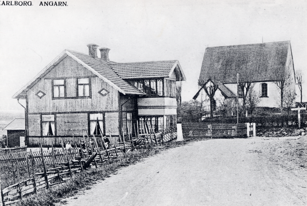 Karlborgs handelsbod  och  Angarns kyrka.   Möjligen sitter familjen  Lundin  framför husgaveln ????

Uppgift om fotoår saknas, men troligen första delen av 1900-talet. Karlborgs handelsbod öppnades av Carl August Lundin 1901.