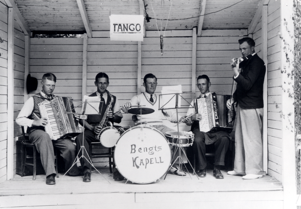 Bengts kapell från Frösunda spelar på festplatsen Arkadien i Rimbo. I spelhytten sitter fr v Erik Fransén  dragspel, Karl-Erik Helgöstam saxofon, Harry Eriksson trummor, kapellets ledare Bengt Helgöstam dragspel och Holmfrid "Julle'"Juliusson fiol.  I spelhyttens tak sitter en skylt som visar vilken dans som spelas – på bilden tango.  Orkestern spelade också på andra dansbanor i trakten