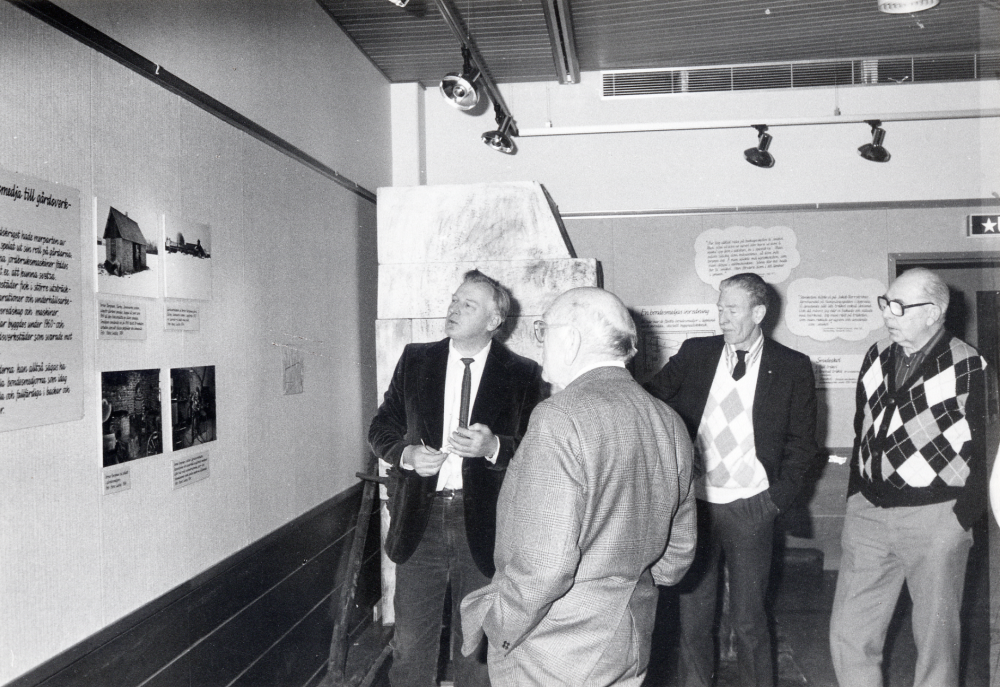 Hans Lustig har sammanställt och tillverkat träfigurer och teckningar i utställningen SMIA i Vallentunasalen. I samband med utställningen berättar han om utställningen och gamla smidestraditioner i programmet En kväll i bondesmedjan. Fr vr Hans Lustig, Gustav Nilsson, Fred Berglund och Åke Ekström. Utställningen kommer från Uplandsmuseet i Uppsala