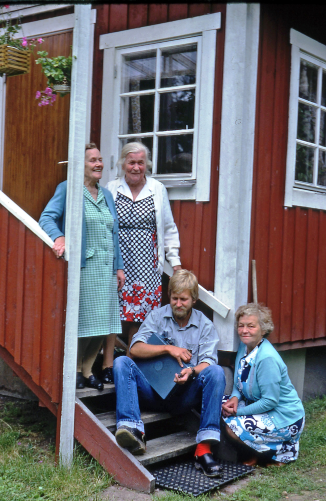 En arbetsdag med lantbrevbärare Mikael Mattsson. Lantbrevbäring i Björklunda; Lantbrevbärare Mikael Mattsson sitter på Hilma Petterssons trappa i Björklunda. Hilma Pettersson sitter på huk nedanför trappan medan hennes väninnor står längre upp på trappan.