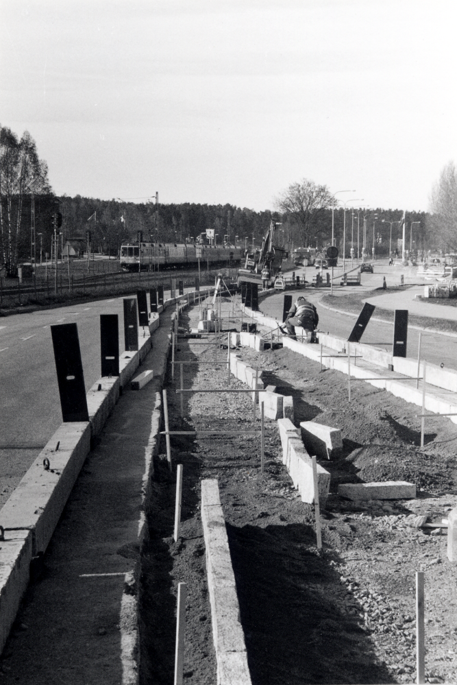 Banvägen i Vallentuna centrum byggs om våren 2000.  Här syns arbeten med stenkanter.  Vid infarten till Centrumpassagen byggs en rondell.  T v syns Roslagsbanans tåg på väg norrut.  Ombyggnadsarbetena har förorsakat problem för bil- och busstrafiken genom centrum