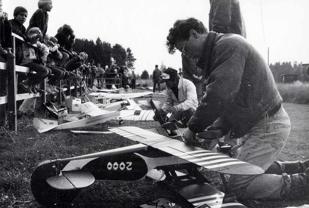 Medlemmar i Vallentuna modellflygklubb har uppvisning på planen mittemot Rosendals industriområde.  Här trimmas planen inför flygningen.  På staketet t h sitter fr höger Johan Böök, Ola Orling? och Magnus Hillbo